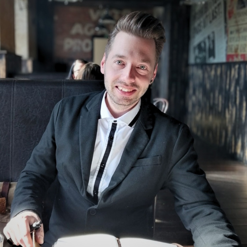 Kevin Böttcher, Experte für Webdesign Erzgebirge, sitzt mit einem Notizbuch am Tisch und lächelt in die Kamera.